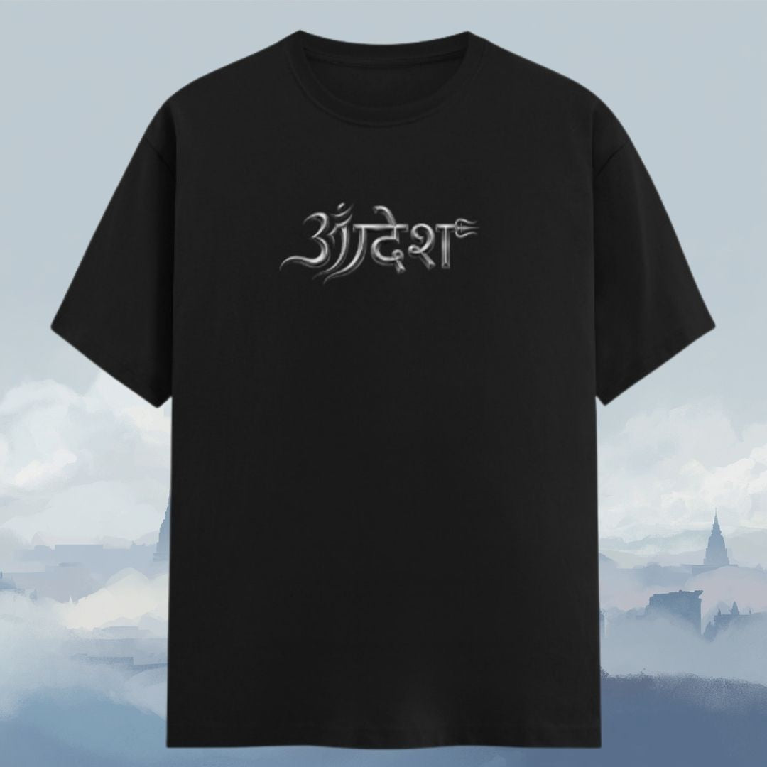 A black short-sleeve t-shirt with a stylized white Sanskrit script graphic on the chest, displayed against a soft, misty blue-gray background.